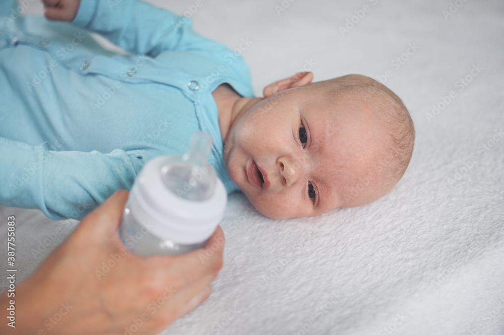 Cute emotional funny newborn infant boy laying on bed with milk bottle. Baby facial expressions.