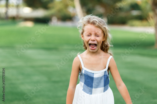 Beautiful sad little blonde curly hair girl crying, on summer background. Concept relationships with children and friendship in school and babygarden .Child crisis .Copy space