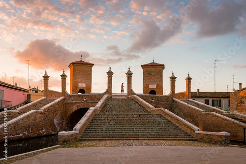 Comacchio, Ferrara / Italy - August 2020: Trepponti Bridge in Comacchio at dawn with a tourist in the center of the columns, sky with clouds photo