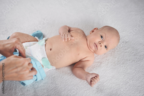 Mom dresses cute emotional funny newborn little infant baby boy in blue jumpsuit