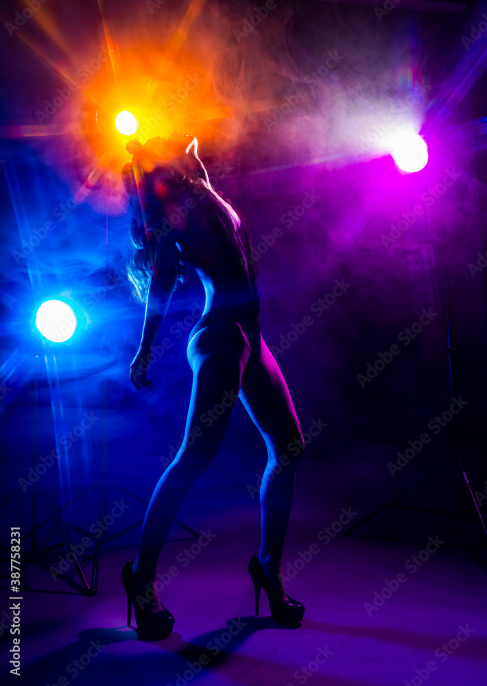 Beautiful slim sexy dancer girl wearing lingerie and high heels posing in the rays of light in a colorful smoke. Artistic, conceptual, silhouette,commercial and advertising design Beautiful slim sexy dancer girl wearing lingerie and high heels posing in the rays of light in a colorful smoke. Artistic, conceptual, silhouette,commercial and advertising design