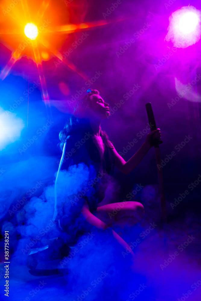 Beautiful slim sexy girl wearing lingerie and high heels posing holding katana sword in her hand in the rays of light in a colorful smoke. Artistic, conceptual, silhouette and advertising design