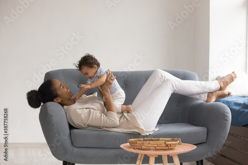 Overjoyed young African American mom have fun with small cute ethnic baby toddler relax together at home. Happy biracial mother play with little child, engaged in funny activity, rest on couch.