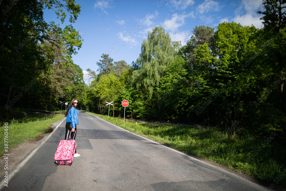 Fototapeta premium The teenager returns on foot along the asphalt road among lush greenery - wonderful trees and shrubs.