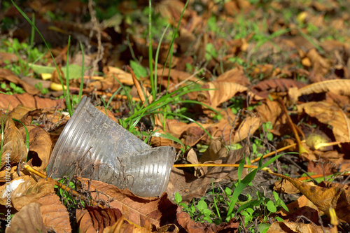 used plastic cup on the ground, litter in the forest on an autumn day on blurred background of dry leaves and green grass, selective focus