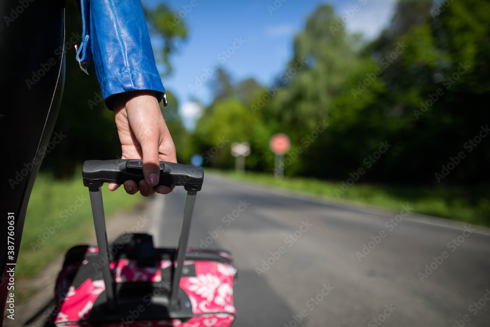 A young female hand holds a black handle from a pink suitcase on wheels and everything seen up close.