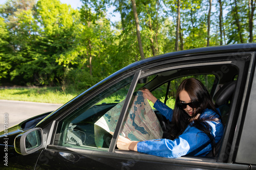 A young girl sits in a car parked on the side of the road in the woods and reads a map to find the right route to its destination.