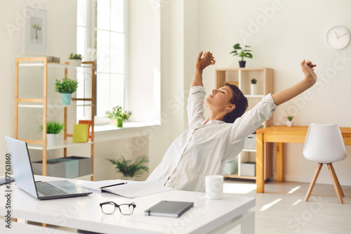 Business woman sitting at office desk, taking break from work and stretching stiff, tense muscles photo
