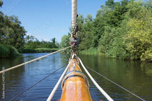 The bowsprit of a sailing yacht on a sunny tree lined river photo