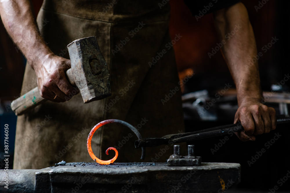 Blacksmith is processing a hot metal object of a spiral shape on the anvil in a dark forge Blacksmith is processing a hot metal object of a spiral shape on the anvil in a dark forge