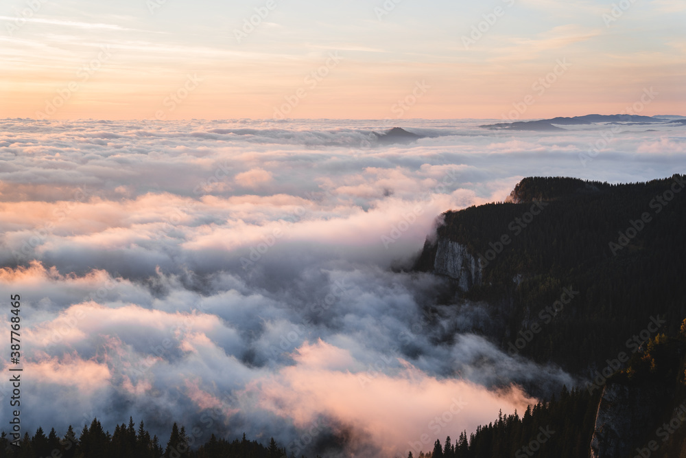 Stunning top view with mist over forest and mountains at sunrise. Colorful landscape with forest in low clouds, mountains peaks above fog, orange sky with sun in the morning in fall. Top view. Nature Stunning top view with mist over forest and mountains at sunrise. Colorful landscape with forest in low clouds, mountains peaks above fog, orange sky with sun in the morning in fall. Top view. Nature