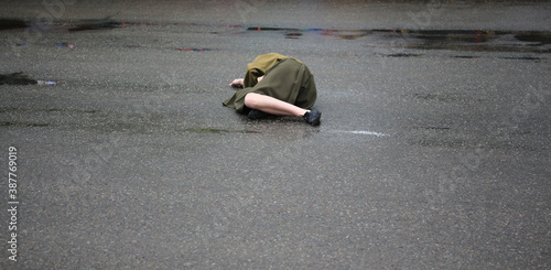 Young woman lying down on ground. Sick or ill girl unconscious outside on the wet asphalt. Victim of force abuse. A crime. Concept image