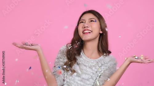 Cute asian women in christmas hats  looking at camera isolated over pink background.young asian woman smile in christmas, new year, valentine day, birthday celebration concept.she play with confetti.