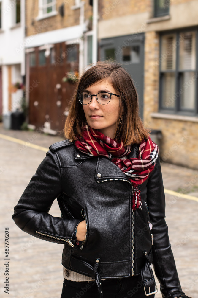 Portrait of an attractive young female wearing a black leather jacket, a red scarf and glasses in a small alley in London, United Kingdom Portrait of an attractive young female wearing a black leather jacket, a red scarf and glasses in a small alley in London, United Kingdom