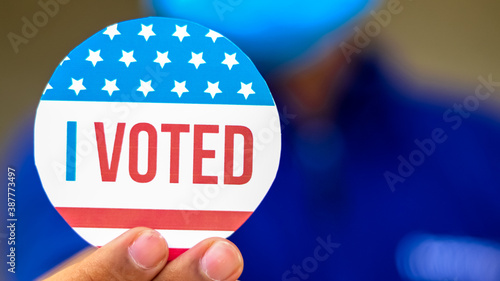 Man from minority group holds I Voted sticker upclose to the camera rackfocus.