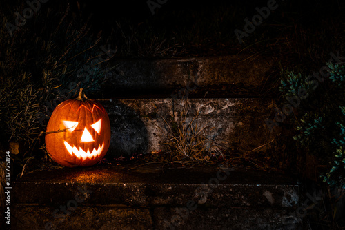 Spooky Halloween pumpkin lantern on concrete stairs in the garden at night