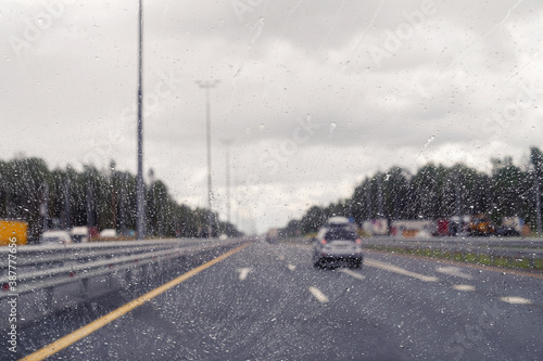 Road view through windshield car window with going rain drops during driving at speed. Unfocused highway. Autumn