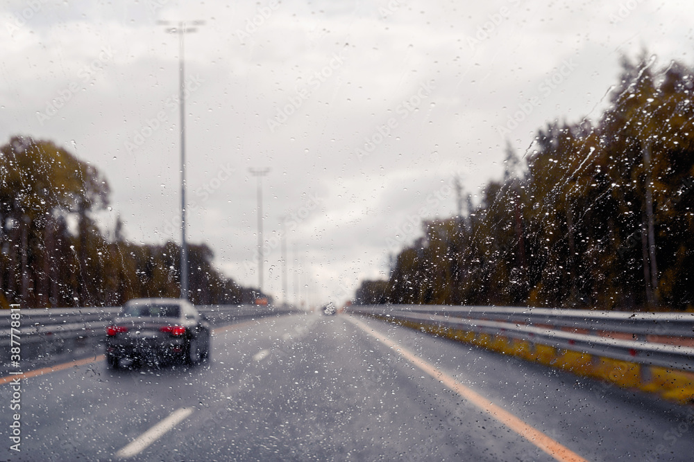 Road view through windshield car window with going rain drops during driving at speed. Unfocused highway. Autumn