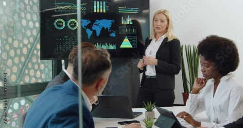 Beautiful confident experienced stylish businesswoman holding a meeting using digital whiteboard with depicted charts in front of multiracial subordinates in confernece room photo