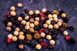 Close-up of 4 kinds of peppercorns on a dark textured surface