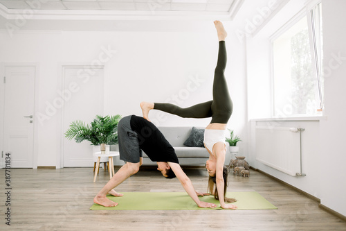 Beautiful sporty fit couple, young man and woman, practicing yoga together at home, doing paired gymnastic yoga asana exercises at home. Balance, meditation and yoga concept
