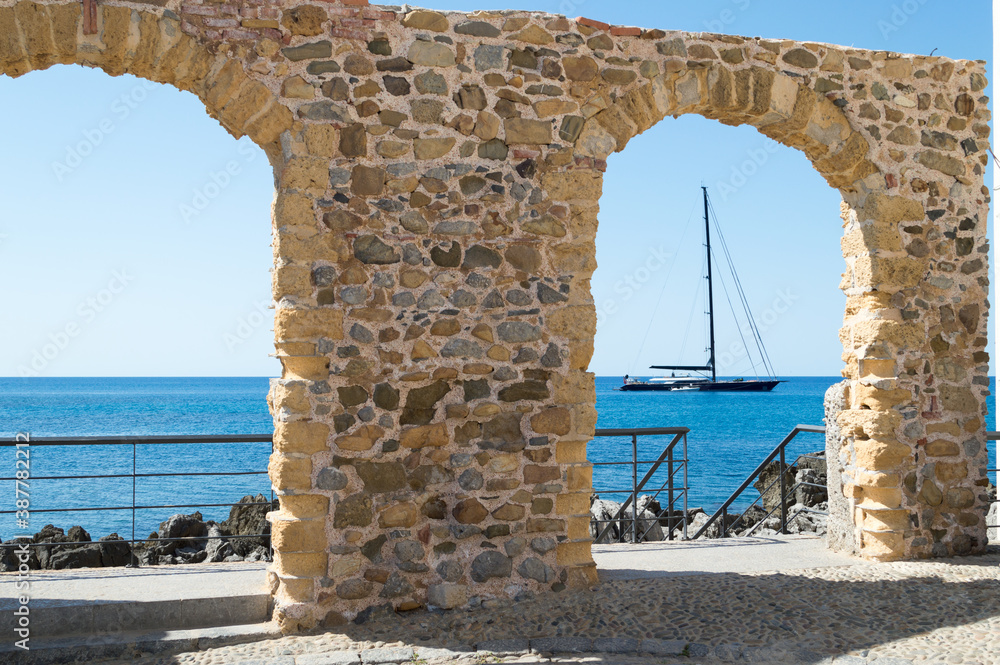 Pictoresque spot in the Cefalù main beach, two old stone arches frame a nice view to the sea, a sail boat is moorde not far away