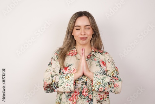 Indoor closeup of beautiful European woman isolated on gray background practicing yoga and meditation, holding palms together in namaste mudra, looking calm, relaxed and peaceful.