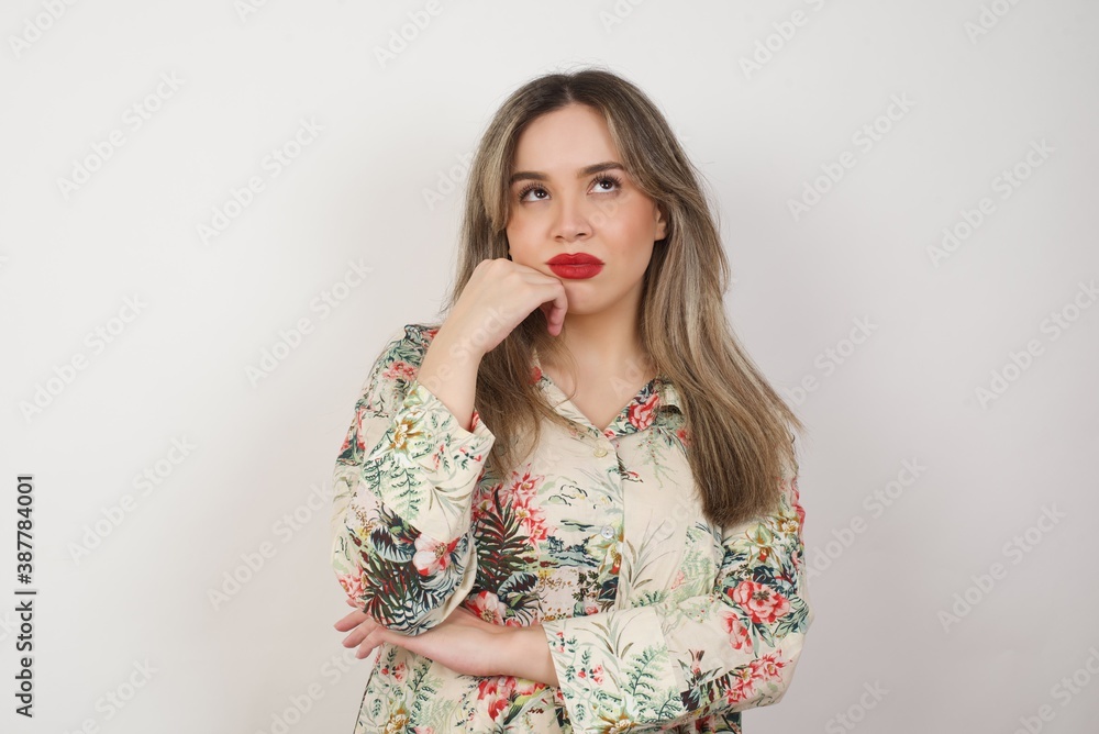 Portrait of thoughtful woman keeps hand under chin, looks away trying to remember something or listens something with interest, dressed casually, poses indoors. Youth concept. Portrait of thoughtful woman keeps hand under chin, looks away trying to remember something or listens something with interest, dressed casually, poses indoors. Youth concept.