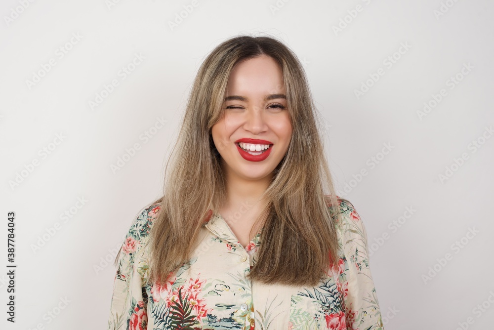 Cute young blonde female blinking her eyes with pleasure having happy expression. Facial expressions and people emotions concept.