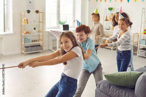 Happy children playing tug-of-war at fun party at home or in leisure club for kids