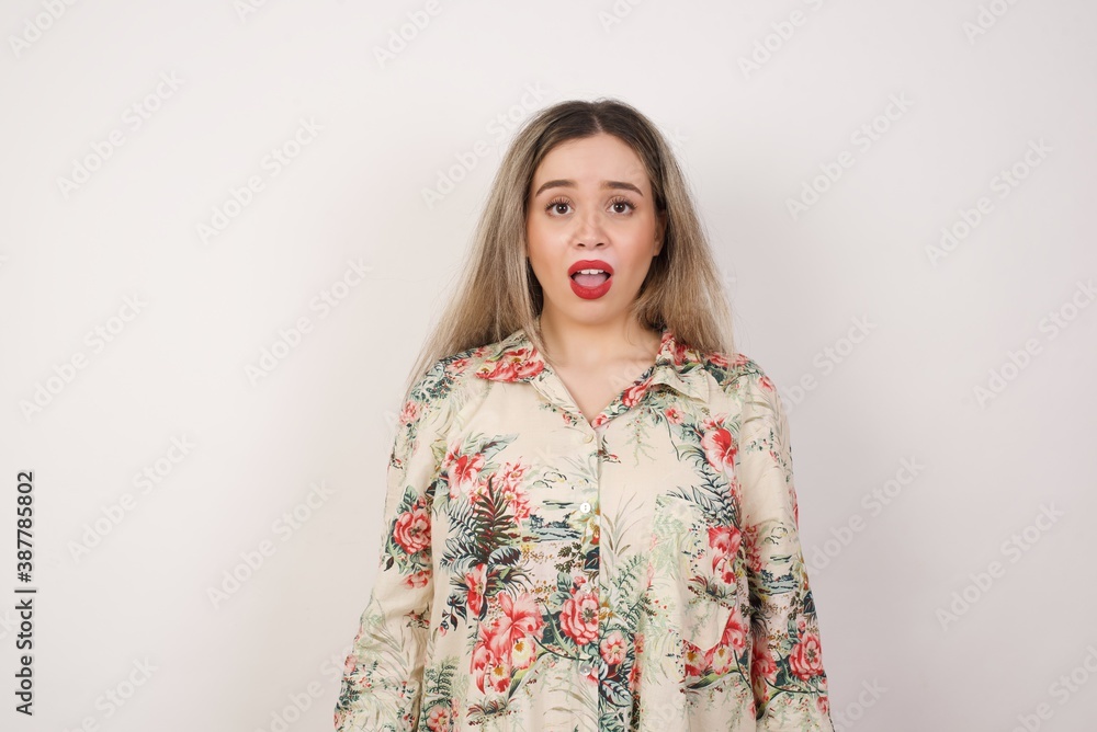 Emotional attractive female with opened mouth expresses great surprisment and frighteness, poses against white concrete background, stares at camera. Unexpected shocking news and human reaction. Emotional attractive female with opened mouth expresses great surprisment and frighteness, poses against white concrete background, stares at camera. Unexpected shocking news and human reaction.