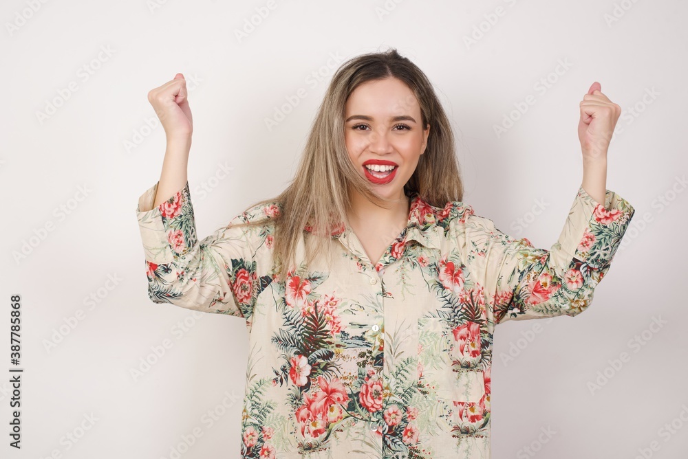 Waist up portrait of strong successful determined young female winner in casual t-shirt raising arms, clenching fists, exclaiming with joy and excitement. Victory, success and achievement concept. Waist up portrait of strong successful determined young female winner in casual t-shirt raising arms, clenching fists, exclaiming with joy and excitement. Victory, success and achievement concept.