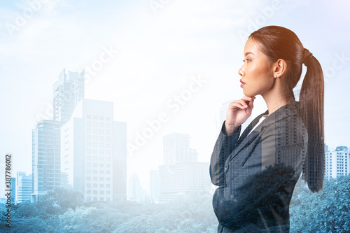 Attractive young Asian business woman in suit with hand on chin thinking how to succeed, new career opportunities, MBA. Bangkok on background. Double exposure.