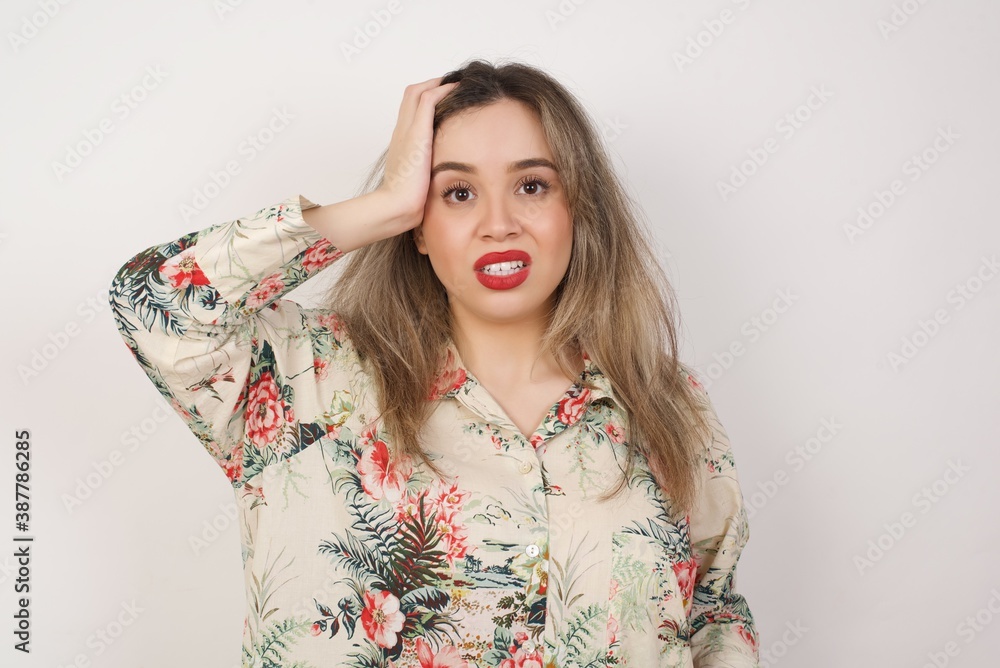 Worried and anxious woman can not remember anything. Portrait of confused cute girl wearing casual clothes, holding hand on hair and frowning, panicking, losing memory over gray wall