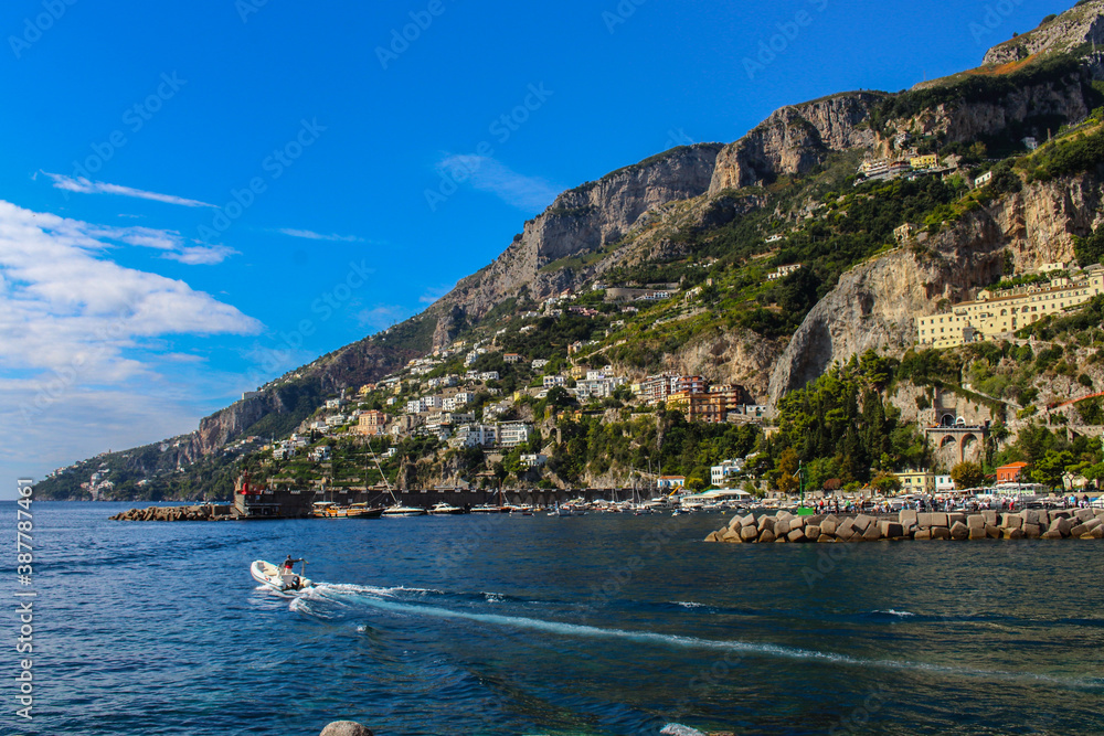 View of the town of Amalfi from the jetty with, the sea, boats and colorful houses on the slopes of the Amalfi coast in the province of Salerno, Campania, Italy.