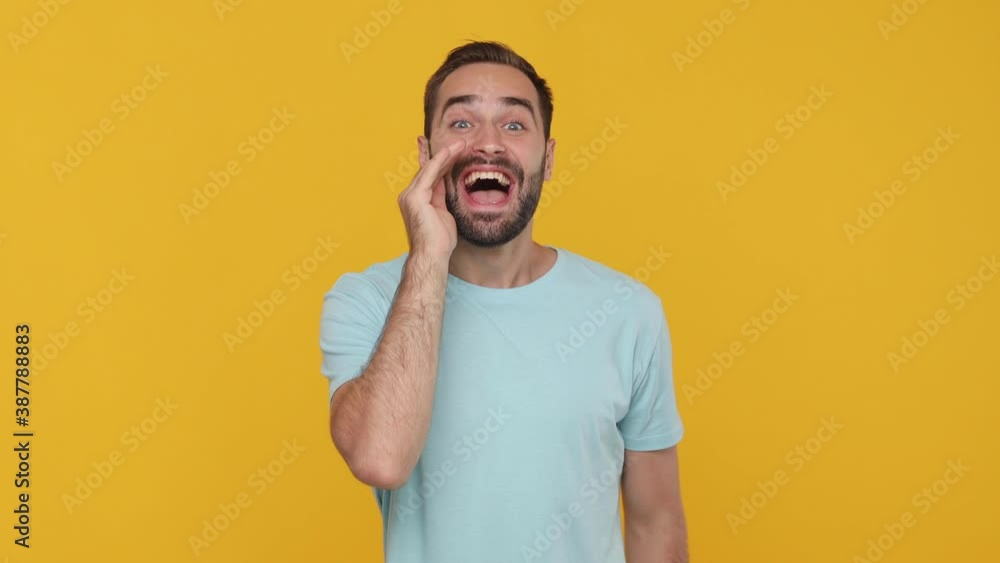 Bearded young man 20s in basic casual blue t-shirt isolated on yellow background studio. People emotions lifestyle concept. Looking at camera shout screaming hot news with hand near mouth shocked wow Bearded young man 20s in basic casual blue t-shirt isolated on yellow background studio. People emotions lifestyle concept. Looking at camera shout screaming hot news with hand near mouth shocked wow