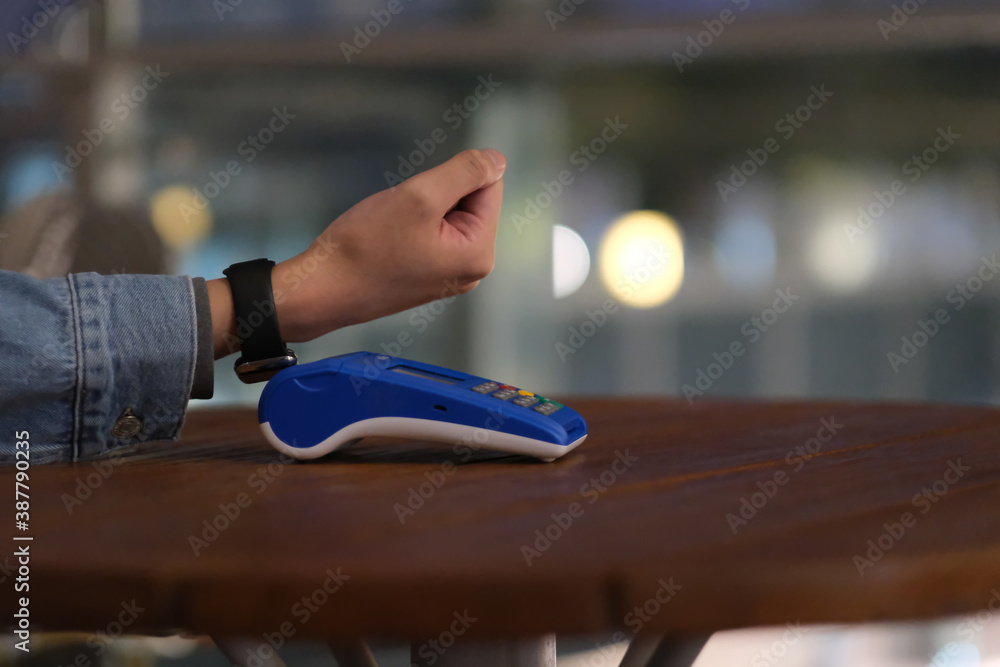 close up hand using smart watch to pay over pos terminal on table at night. bokeh background