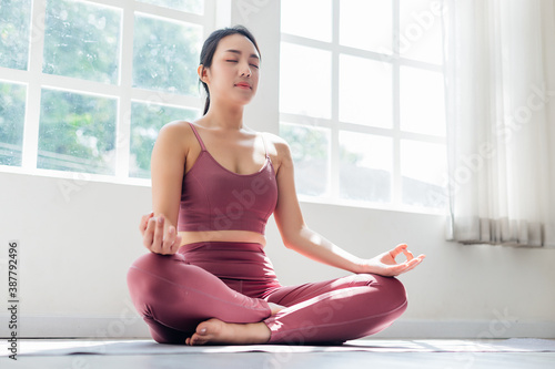 Young attractive smiling woman practicing yoga, sitting in Half Lotus exercise at home. Concept of healthy life and natural balance between body and mental development. Full length