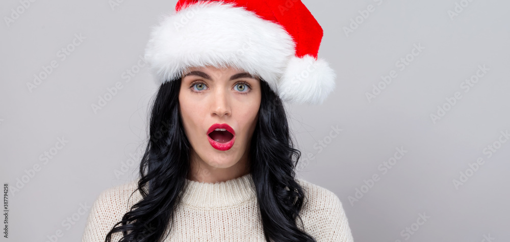 Surprised young woman in a Santa hat on a gray background Surprised young woman in a Santa hat on a gray background
