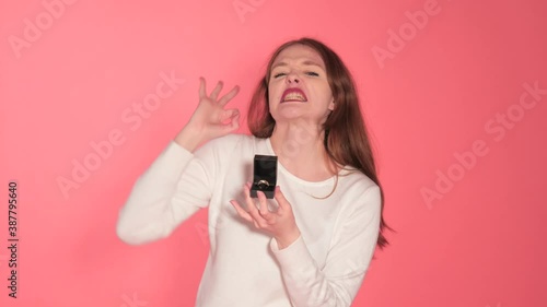 Young Woman Selling Ring To Camera Against Studio Background 