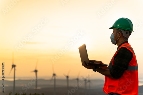 Young maintenance engineer working in wind turbine farm at sunset