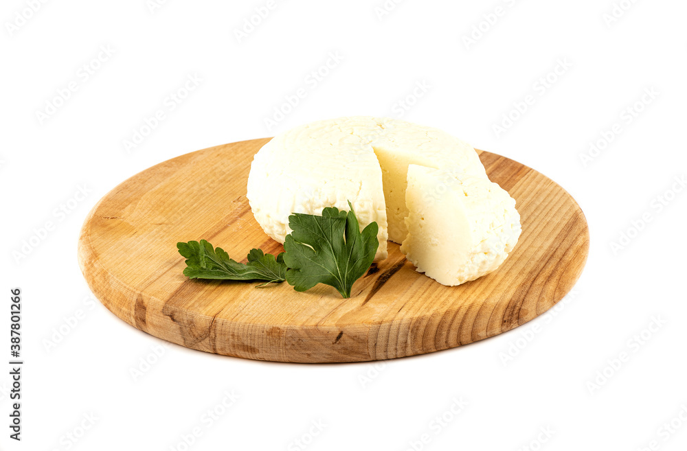 Round soft cheese and parsley leaf on a wooden cutting board.