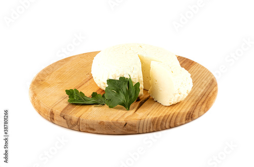 Round soft cheese and parsley leaf on a wooden cutting board.
