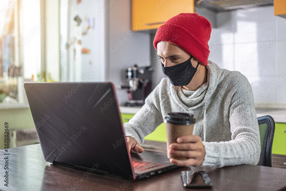 Man in a face mask is using a laptop at home. Concept of remote work, distance communication and lifestyle in a pandemic Man in a face mask is using a laptop at home. Concept of remote work, distance communication and lifestyle in a pandemic