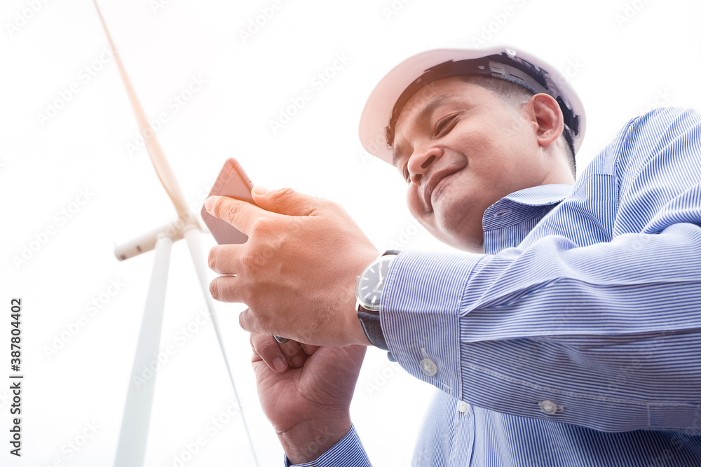 Engineers windmills are working on smartphone with the wind turbine in background Engineers windmills are working on smartphone with the wind turbine in background