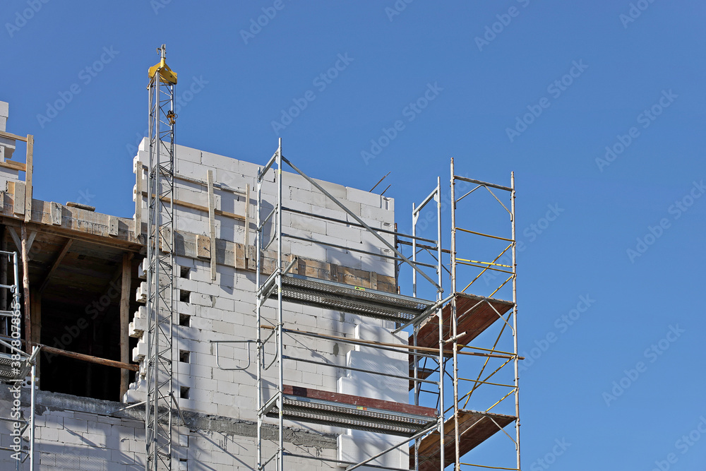 Modern construction forests for workers are leaning against the facade of a high-rise building under construction. Repair and construction work at heights. Safety of human labor. Danger of heights