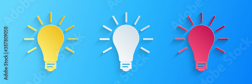 Paper cut Light bulb with rays shine icon isolated on blue background. Energy and idea symbol. Lamp electric. Paper art style. Vector.