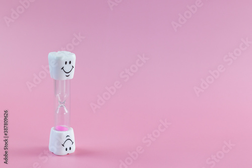 Concept of recommended time for brush teeth. Hourglass. Brushing teeth for 3 minutes. Sand clock with smiley face. Pink background