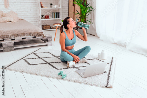 Young fit woman in sportswear drinks water while doing everyday morning warm up exercises on the floor at home. photo