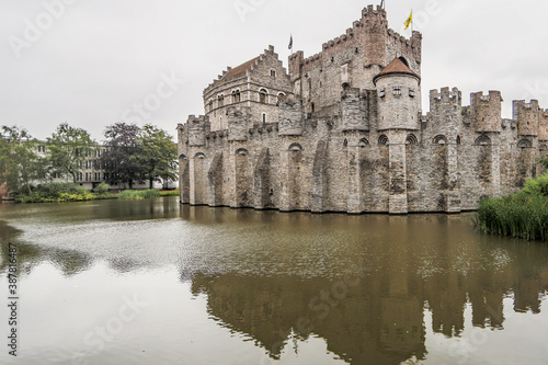 Canal with calm waters surrounding the medieval castle of Gravensteen (Castle of the Counts), reflection and light breeze on the water surface, cloudy day with a gray sky in Ghent, Belgium